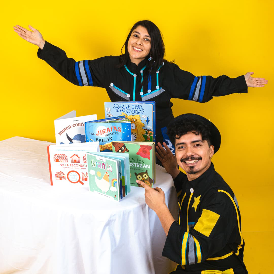 Denis y Pablo mostrando libros infantiles en una mesa con fondo amarillo